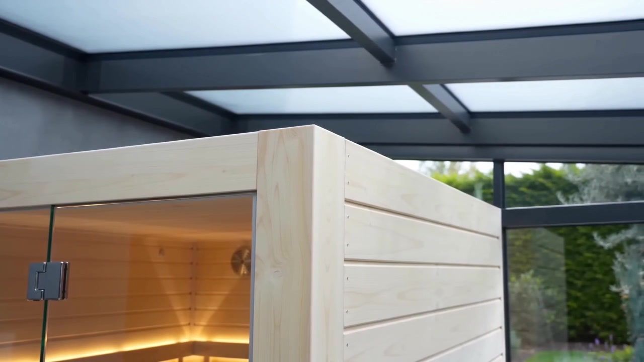 Záběr z videa: sauna ze světlého dřeva pod prosklenou střechou zimní zahrady